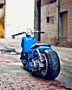 a blue motorcycle parked on the side of a road next to a brick wall and building