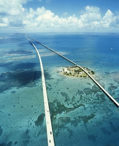 an island in the middle of the ocean with a road going through it and some clouds above