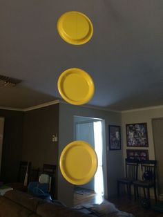 three yellow plates hanging from the ceiling in a living room with chairs and tables behind them