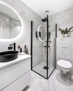 a modern bathroom with white marble walls and flooring, including a round mirror above the shower