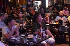 a group of people sitting at tables in a restaurant with food and drinks on the table