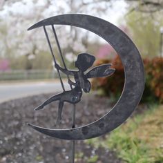 a metal sculpture of a fairy sitting on the moon holding a stick in it's hand