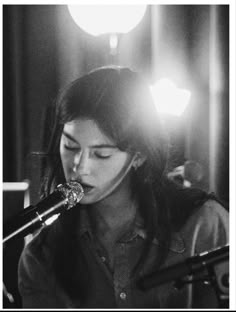 a woman singing into a microphone while standing in front of a microphone with lights behind her