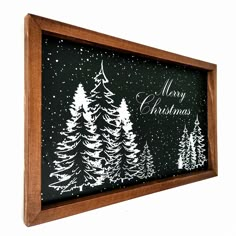 a black and white christmas card hanging on a wall next to a wooden frame with trees painted on it