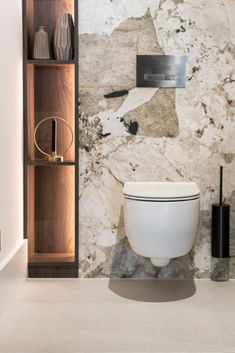 a white toilet sitting inside of a bathroom next to a wooden book shelf filled with vases