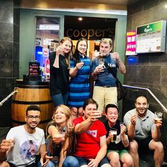 a group of people sitting and standing around each other in front of a building holding beers