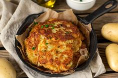 some food is in a black pan on a wooden table next to potatoes and garlic