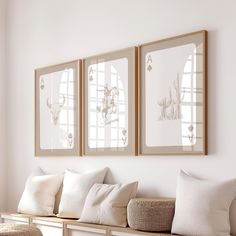 three framed pictures hang on the wall above a white bench with pillows and wicker basket