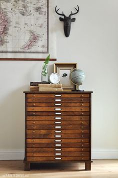 a wooden dresser with drawers and a map on the wall above it, along with an antelope's head