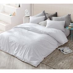 a bed with white sheets and pillows on top of a rug next to a table