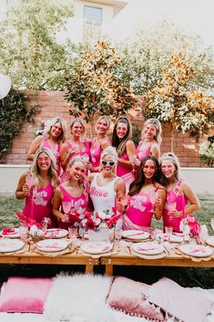 a group of women in pink outfits standing around a table with plates and cake on it