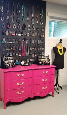 a pink dresser sitting in front of a wall filled with jewelry