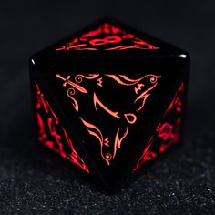 a black and red illuminated dice sitting on top of a dark surface with an intricate design