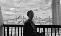 a man standing on top of a balcony next to a tall building with a city skyline in the background