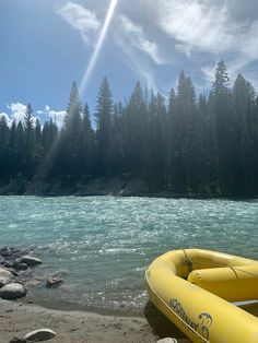 an inflatable raft sitting on the shore of a river with pine trees behind it