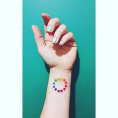 a woman's hand with a small colorful circle tattoo on her wrist