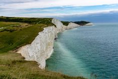 the cliffs are white and have blue water in front of them, along with green grass on either side