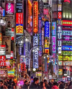 a city street filled with lots of tall buildings covered in neon signs and people walking around