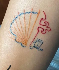 a woman's leg with a tattoo on it that reads 2012 july and an orange, blue, and red fan