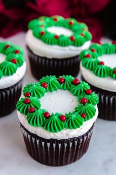 four cupcakes decorated with green frosting and red berries are on a table