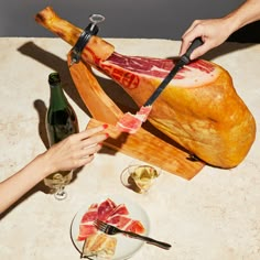 a person cutting up a piece of meat on top of a wooden board next to wine glasses