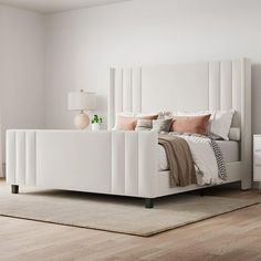 a white bed sitting on top of a hard wood floor next to a dresser and lamp