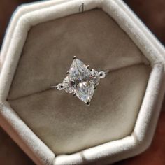 an engagement ring with a princess cut diamond set in a white gold band, on top of a velvet box