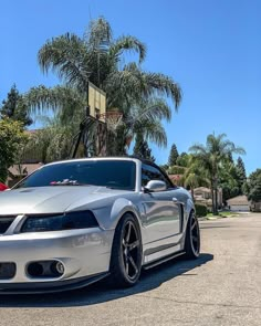 a silver sports car parked in front of a basketball hoop with palm trees behind it