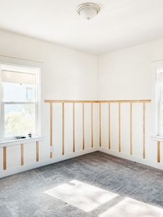 an empty room with white walls and wood trimmings on the wall, in front of two windows