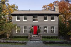 a gray house with red door and steps leading up to the front entrance, surrounded by trees