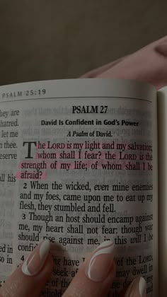 a woman's hand holding an open bible with pink and white nail polish on it