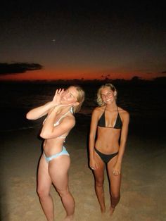 two women in bikinis standing on the beach at night