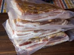 three sandwiches wrapped in plastic sitting on top of a wooden table