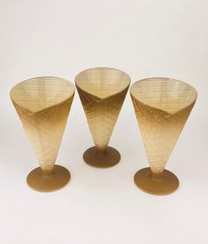 three gold colored vases sitting next to each other on top of a white surface