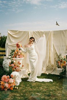 a woman standing next to a cake on top of a lush green field covered in flowers