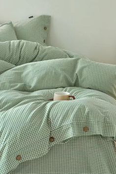 an unmade bed with green and white checkered comforter, pillows and pillow cases