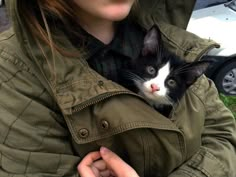 a woman is holding a black and white cat in her arms while wearing a green jacket