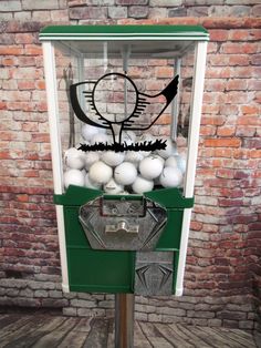 a green and white machine with lots of balls in it's display case next to a brick wall