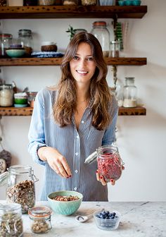 a woman standing in front of a counter holding a jar filled with berries and granola