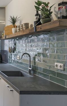 a kitchen with green tiles on the wall and white cupboards next to the sink