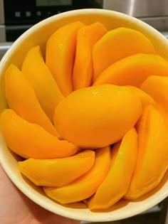 a person holding a white bowl filled with sliced mangoes on top of a counter