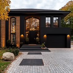 a black house with lots of windows and steps leading up to the front door is lit by lights that are on either side of the garage doors