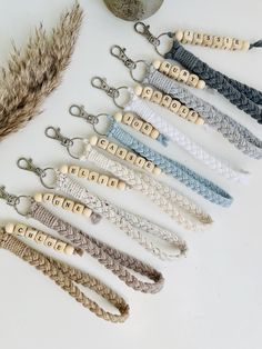 six key chains with wooden beads are lined up on a white surface next to a feather