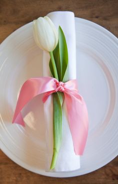 a white plate topped with a pink ribbon and two tulips on top of it