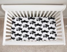 a white crib with a black and white truck design on the bottom, next to a beige carpet