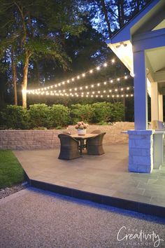 an outdoor dining area with string lights strung over the table and chairs on the patio