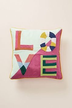 an embroidered pillow with the word love on it, sitting against a pink wall background