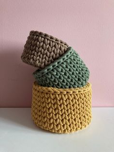 three crocheted hats are stacked on top of each other in front of a pink wall