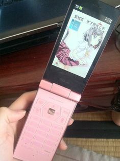 a person holding up a pink cell phone with an anime character on it's screen