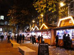 people are walking down the sidewalk in front of christmas lights and shops on a city street at night